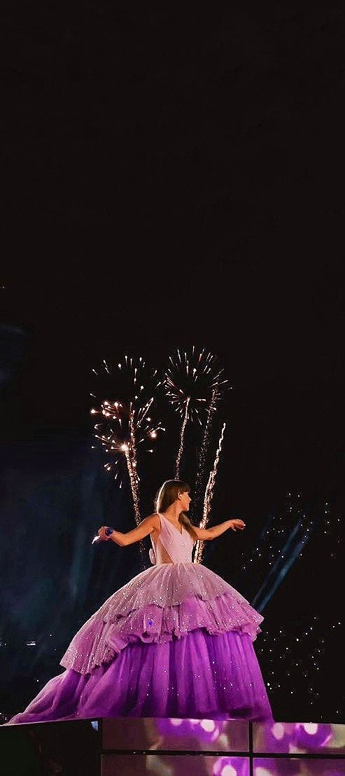 a woman in a purple dress on stage with fireworks