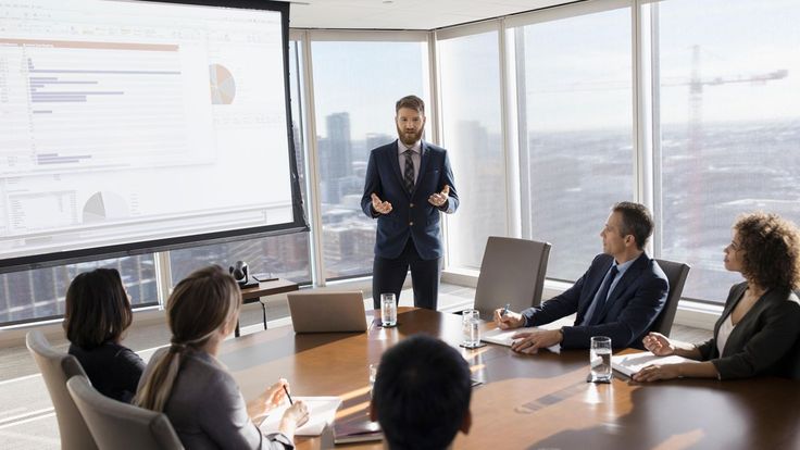 a man standing in front of a group of people sitting around a conference room table