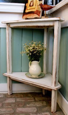 a white vase with flowers on top of a shelf next to a brick floor and wall