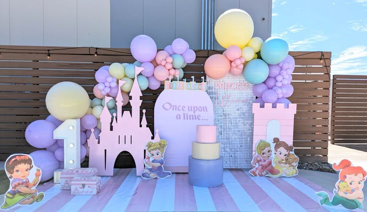 a table topped with lots of balloons and princess themed items in front of a fence