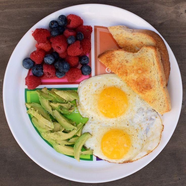 a white plate topped with eggs, toast and fruit on top of a wooden table