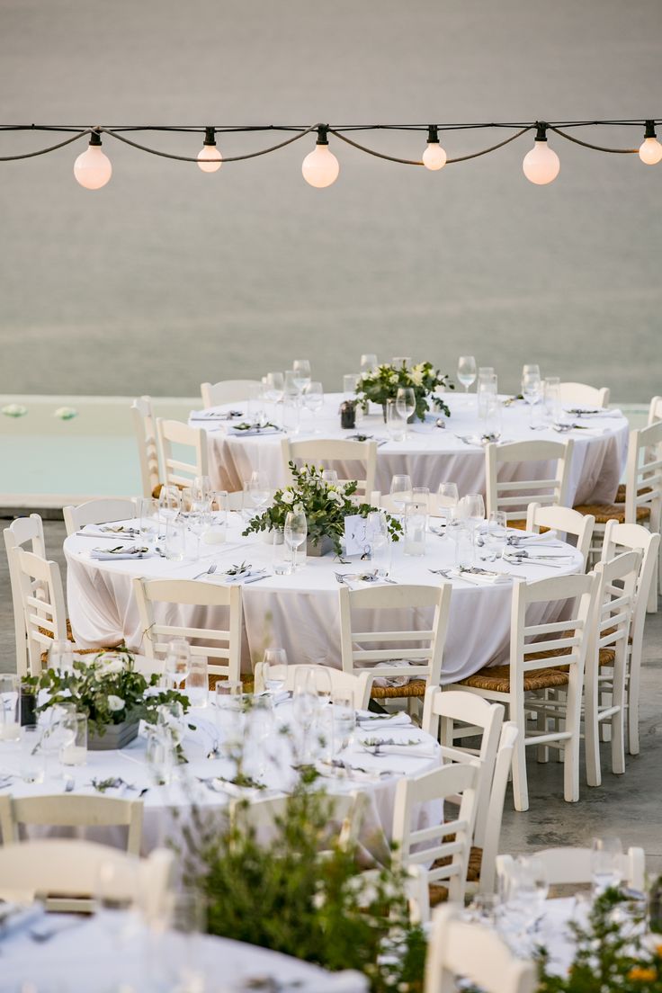 tables and chairs with white linens are set up for an outdoor wedding reception by the water