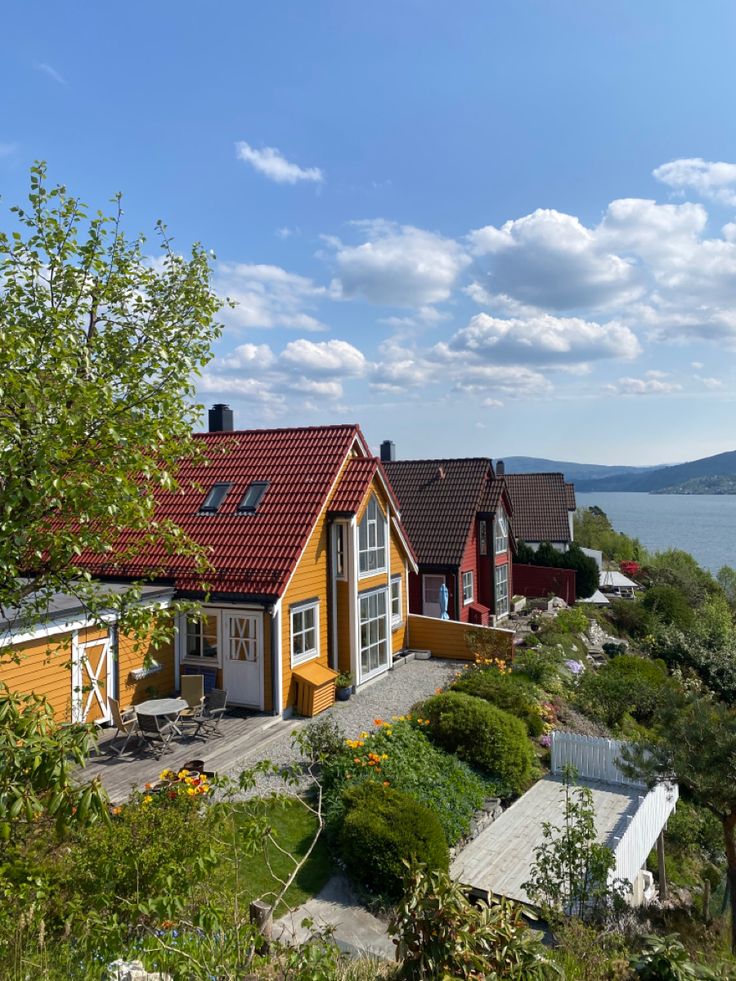 a small yellow house sitting on top of a lush green hillside next to the ocean