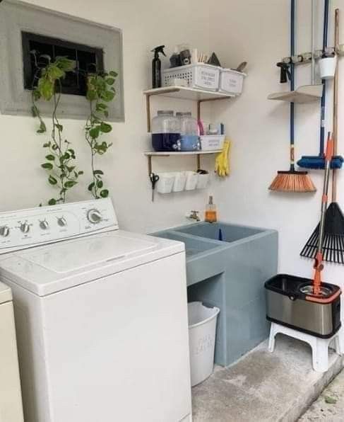 a washer and dryer sitting in a room next to a shelf with brooms on it