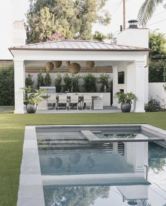 an outdoor dining area next to a pool with chairs and tables on the grass near it