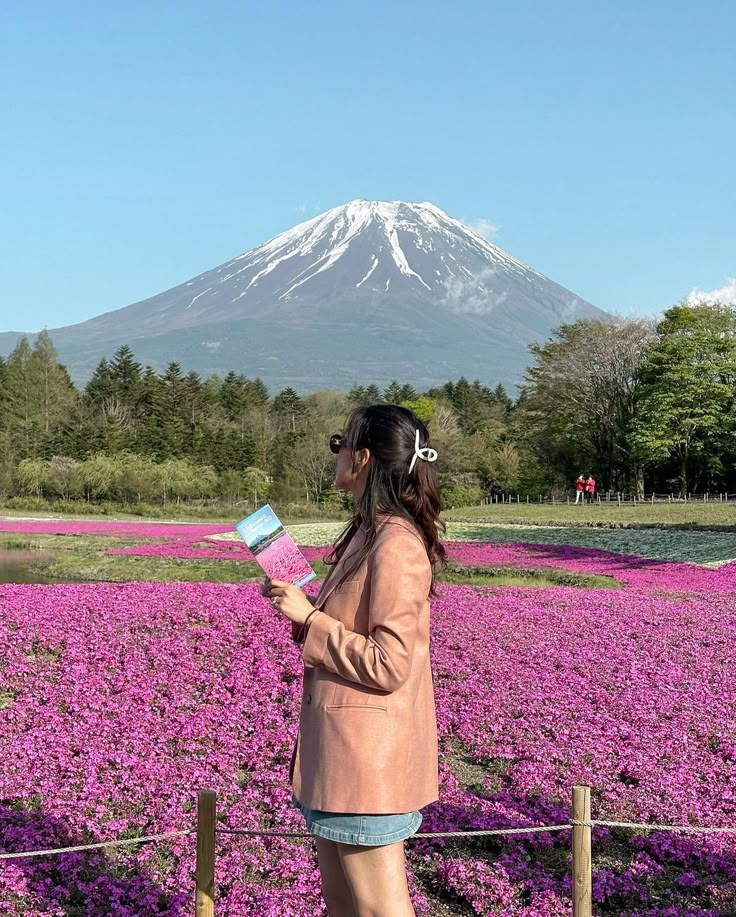 a woman standing in front of a field of purple flowers with a mountain in the background