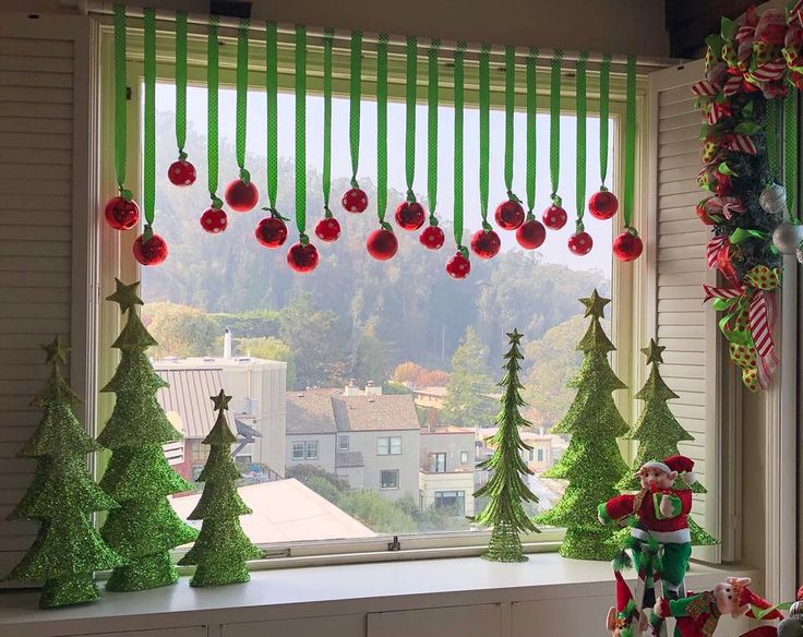 a window with christmas decorations hanging from it's sides and trees on the windowsill