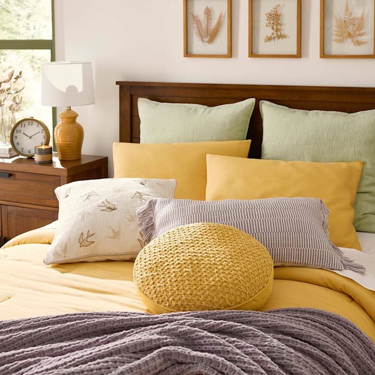 a bed with yellow sheets and pillows in a bedroom next to two clocks on the wall