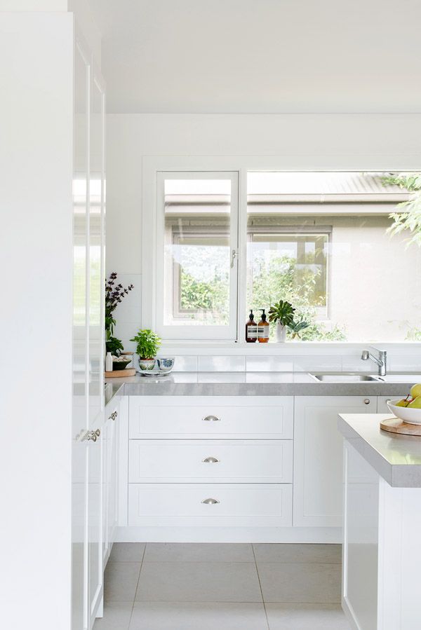 a kitchen with white cabinets and counter tops next to a plant in a vase on the window sill