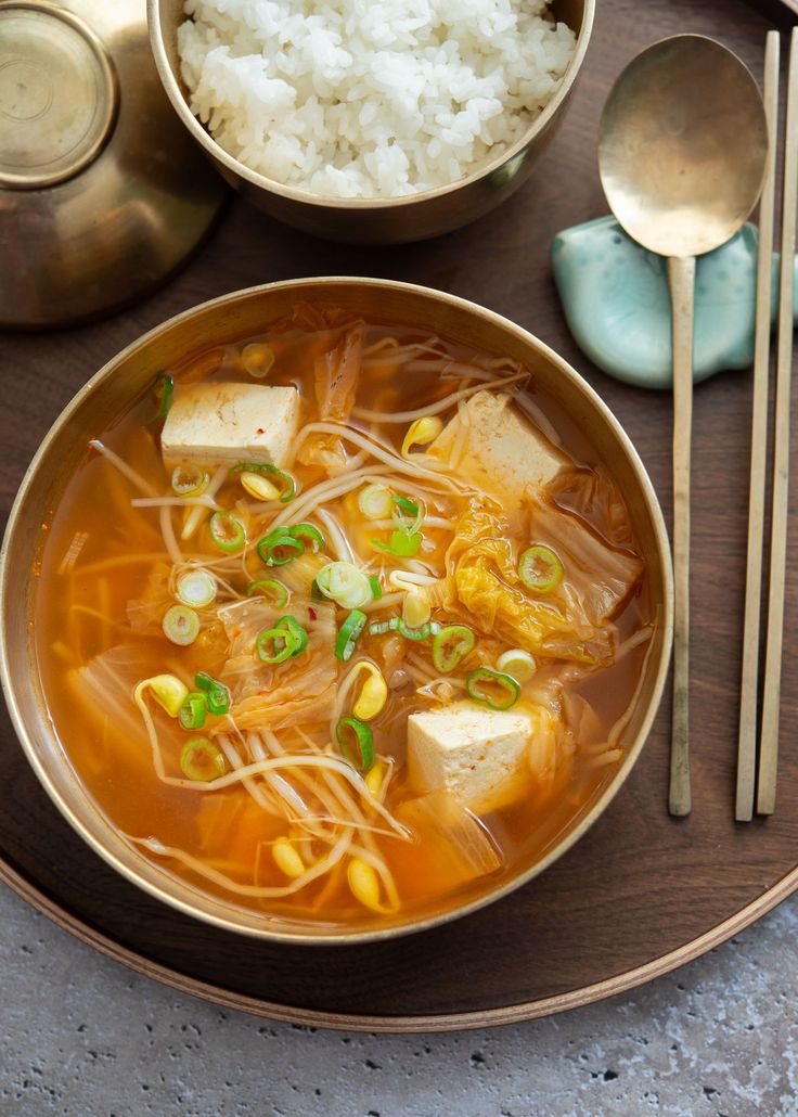 a bowl of soup with tofu, rice and green onions on a wooden plate