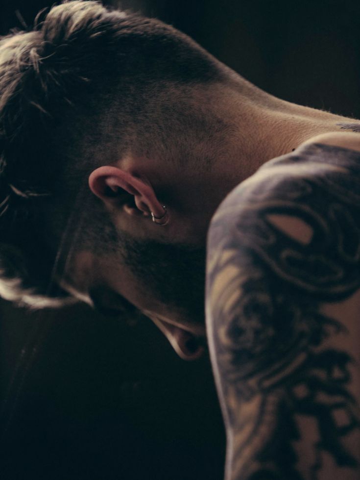 a man with tattoos and piercings on his head looking down at something in the distance