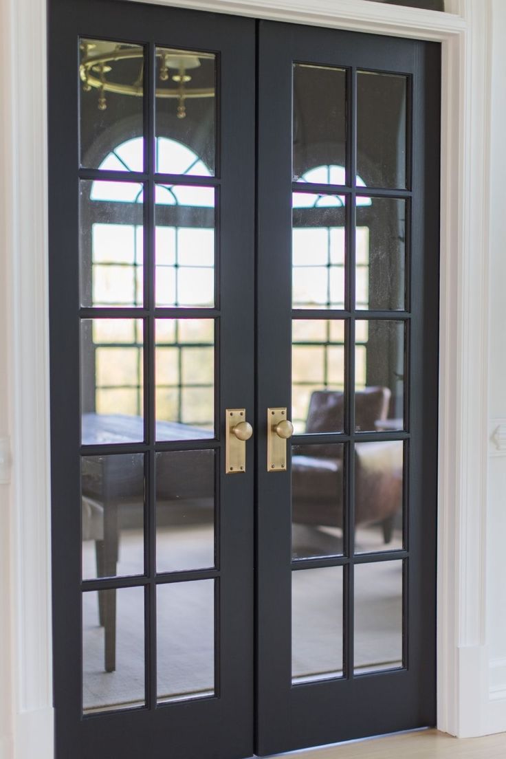 a black double door with glass and gold handles in a living room area that is painted white