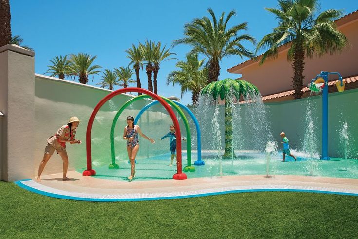 two women playing in the water at an outdoor play area with palm trees and fountains