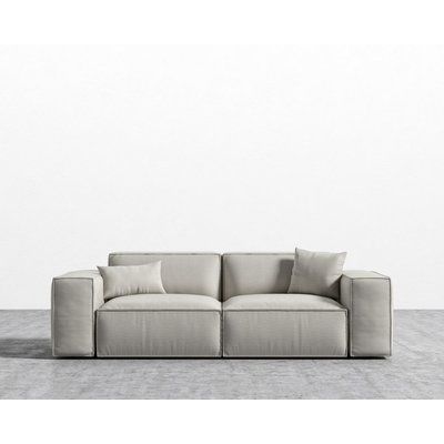 a white couch sitting on top of a gray floor next to a wall with two pillows