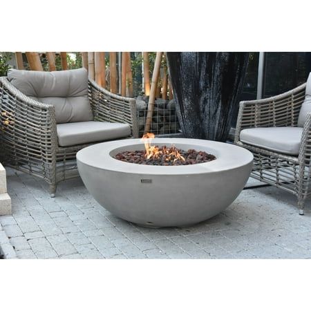 a fire pit sitting on top of a patio next to two chairs and a table