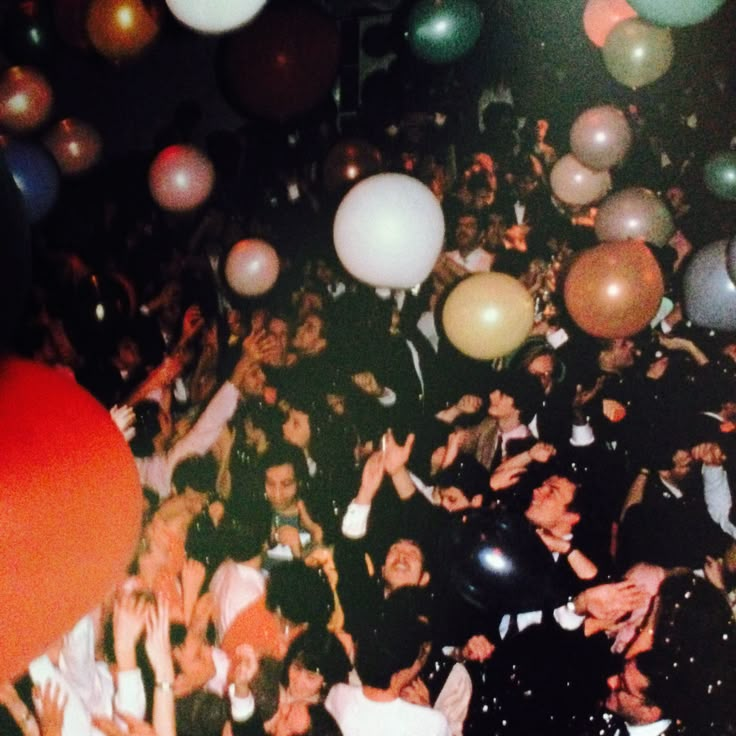 a large group of people standing around each other with balloons in the air above them