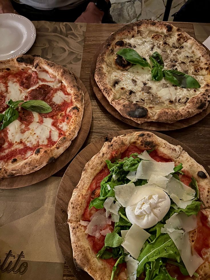 three pizzas with cheese, spinach and other toppings on wooden platters