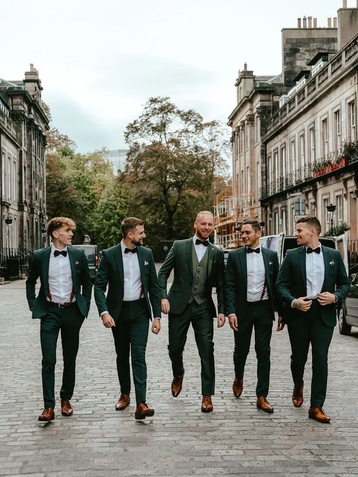 four men in tuxedos are walking down the street with their arms around each other