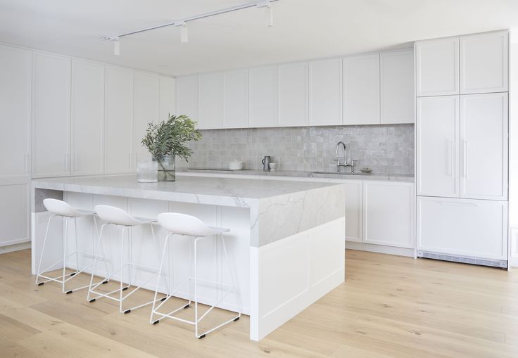 a kitchen with white cabinets and marble counter tops, three stools at the island