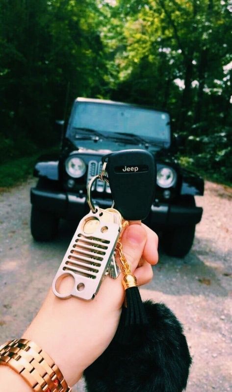 a hand holding a car key chain with a jeep in the background