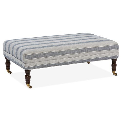 a striped ottoman sitting on top of a white floor next to a wooden leg rest