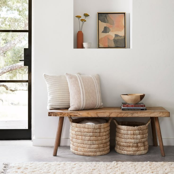 a wooden bench sitting next to a window in a living room with two baskets on top of it