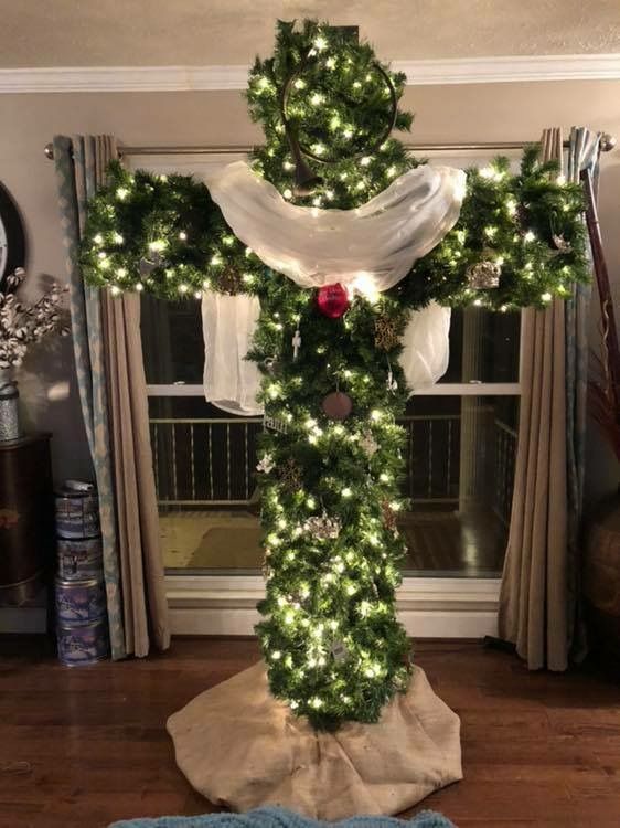 a cross decorated with christmas lights in the middle of a room next to a window