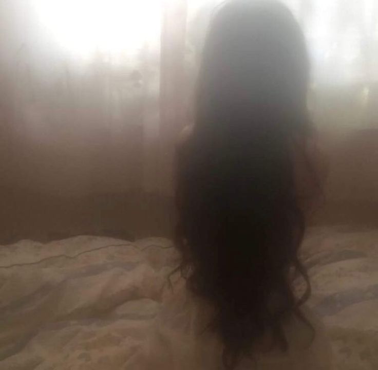 the back of a woman's head sitting on a bed in front of a window