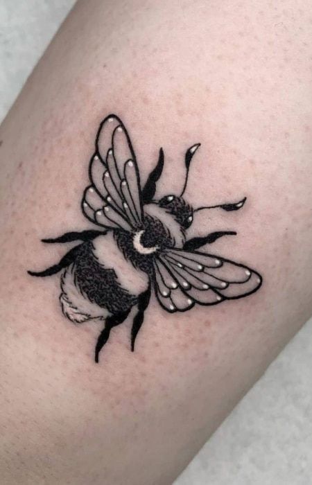 a small black and white bee tattoo on the leg, it looks like he is flying