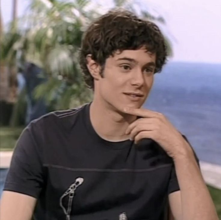 a young man sitting in front of an ocean