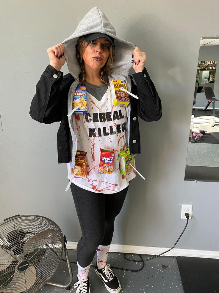 a woman standing in front of a wall wearing a hoodie and eating cereal t - shirt