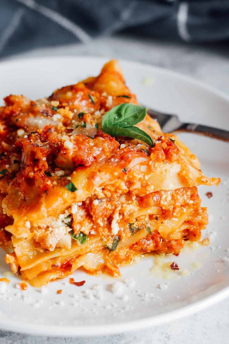 a white plate topped with lasagna covered in sauce and cheese next to a fork