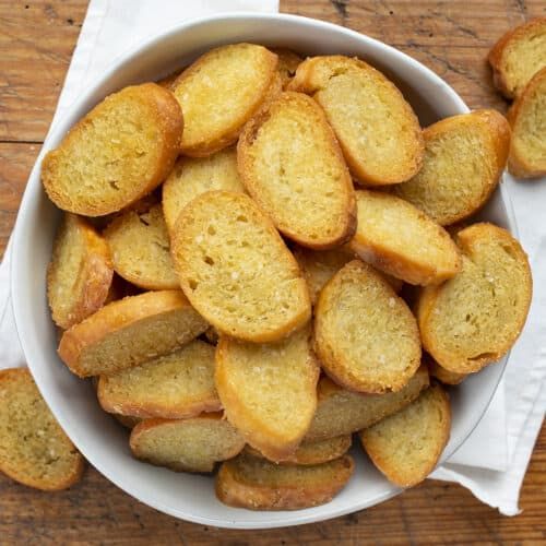 a white bowl filled with fried bread on top of a wooden table next to a napkin