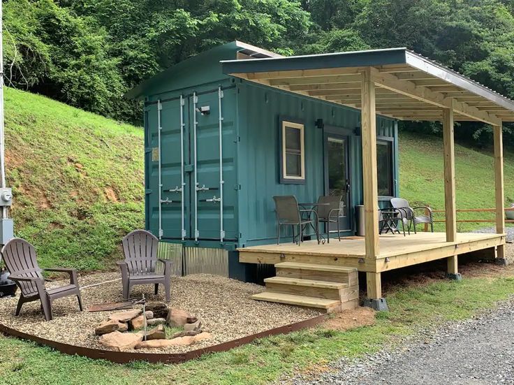 a small blue container home sitting on top of a lush green hillside next to a fire pit