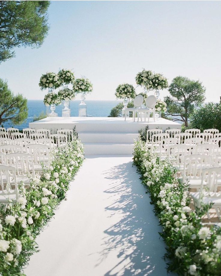 an outdoor wedding setup with white flowers and greenery at the end of the aisle