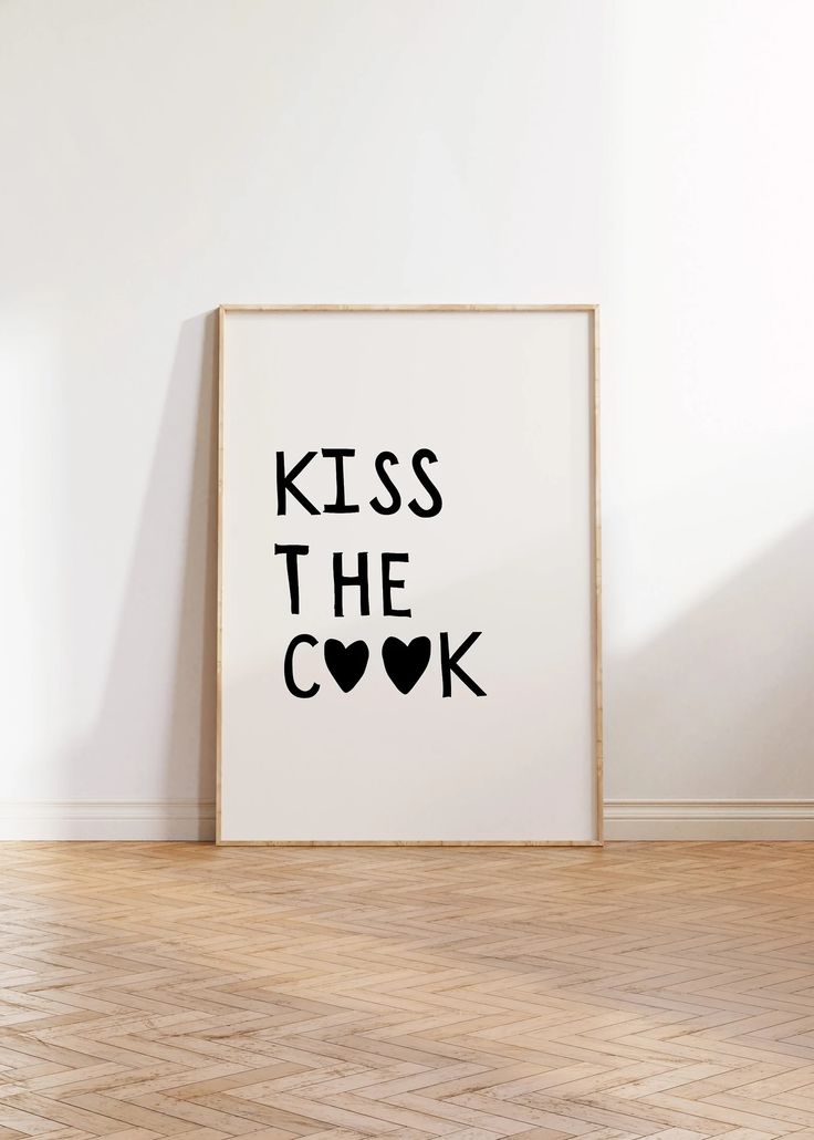 a black and white poster with the words kiss the cook on it in front of a wooden floor