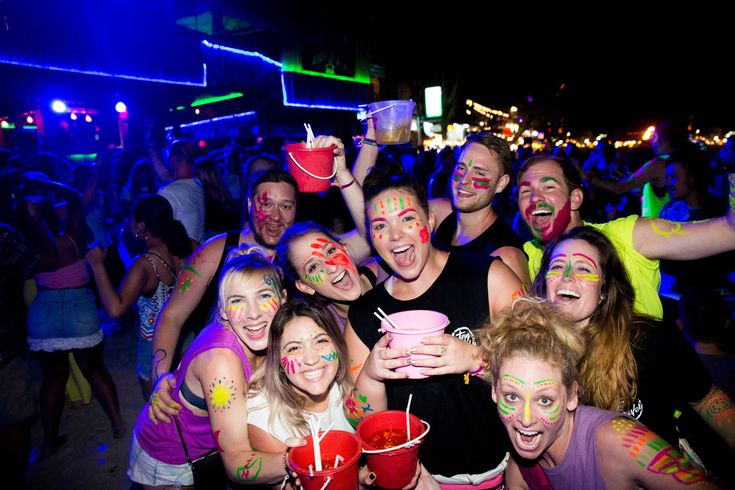 a group of people with their faces painted in different colors and holding drinks at a party