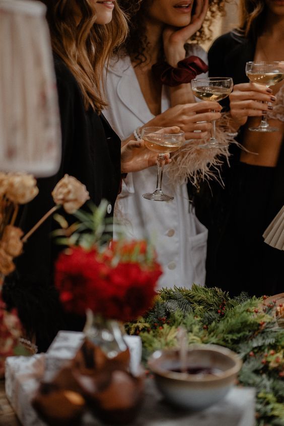 three women are holding wine glasses at a table with flowers and greenery on it