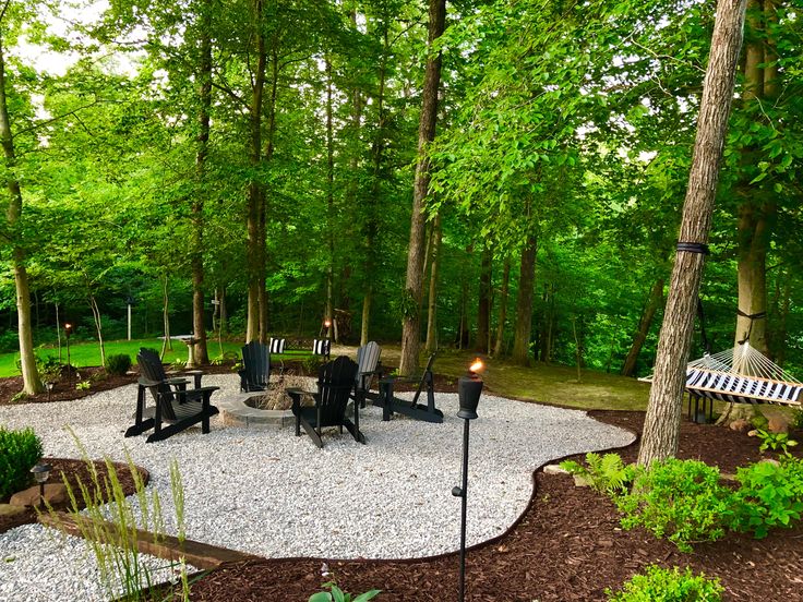 an outdoor patio with gravel and chairs in the middle, surrounded by green trees on both sides