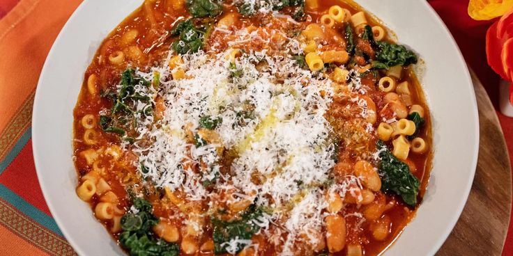 a bowl of pasta with spinach and parmesan cheese on top, sitting on a table