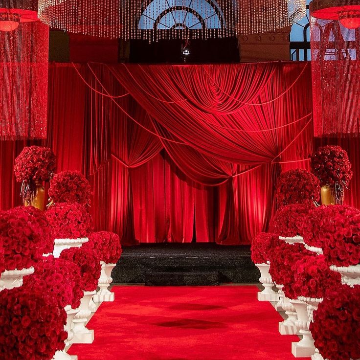 a red and white wedding set up with flower arrangements on the aisle, flowers in vases at the end