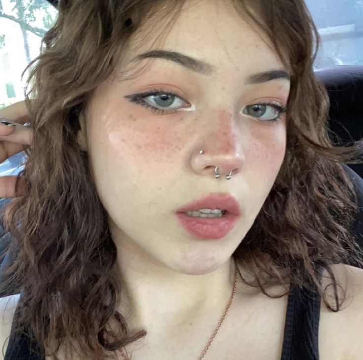 a woman with freckles and piercings on her nose looking at the camera