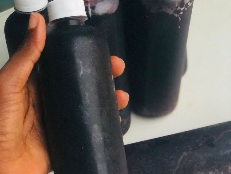 a hand holding a black bottle with two white caps on it and another one is empty