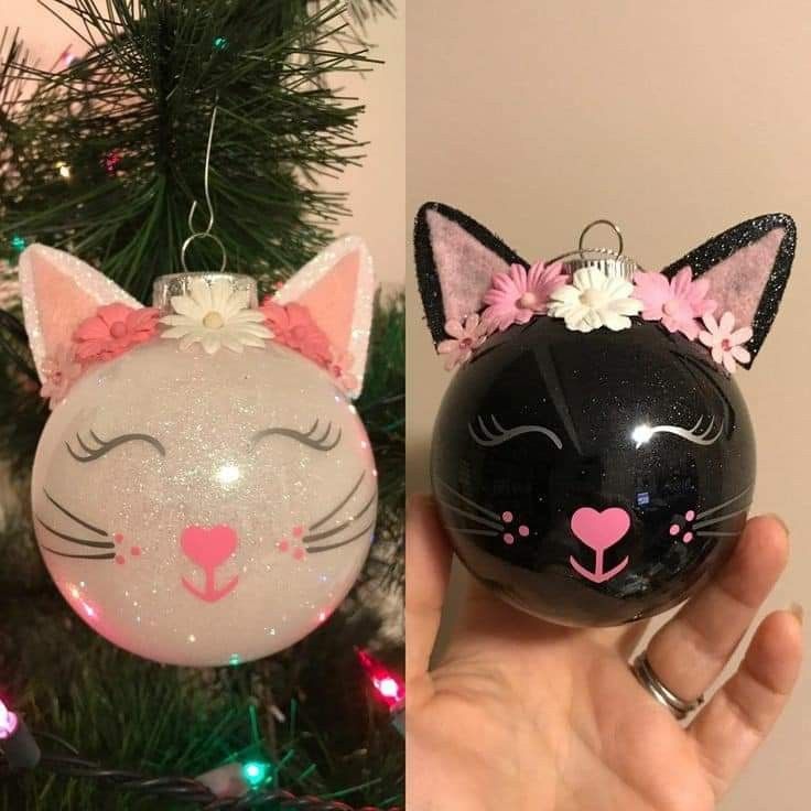 a hand holding a black and white cat ornament next to a christmas tree