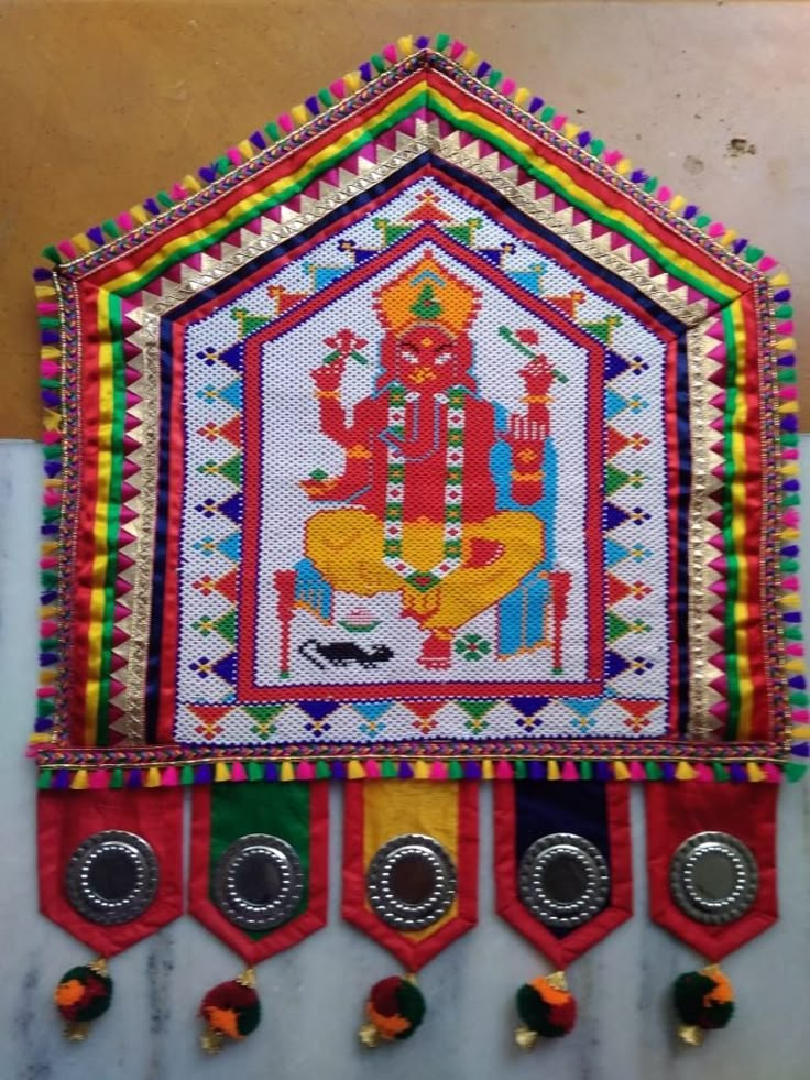 an embroidered wall hanging with buttons and beads on the bottom, depicting a god in colorful colors