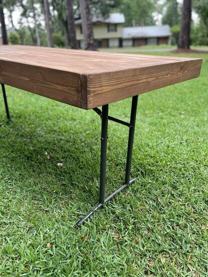 a wooden table sitting on top of a green grass covered field with trees in the background