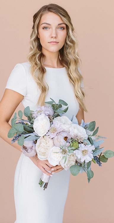 a woman in a white dress holding a bridal bouquet with greenery and flowers