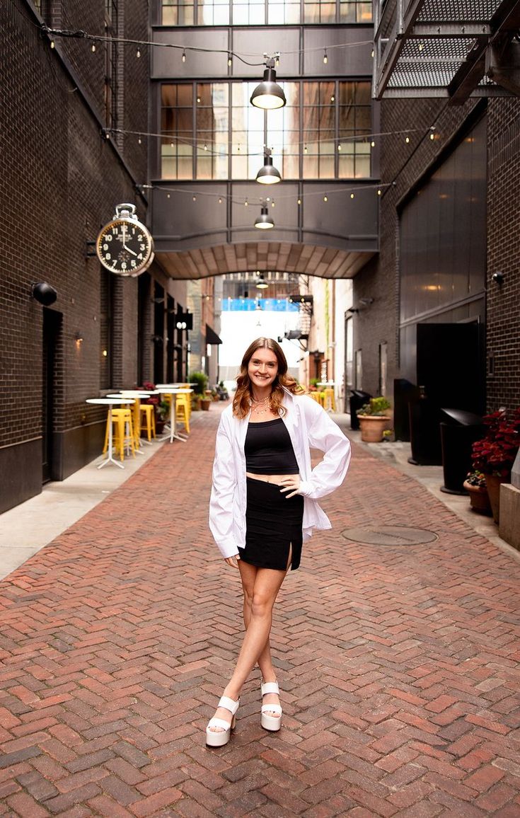 a woman is standing in the middle of an alley way with a clock hanging from the ceiling