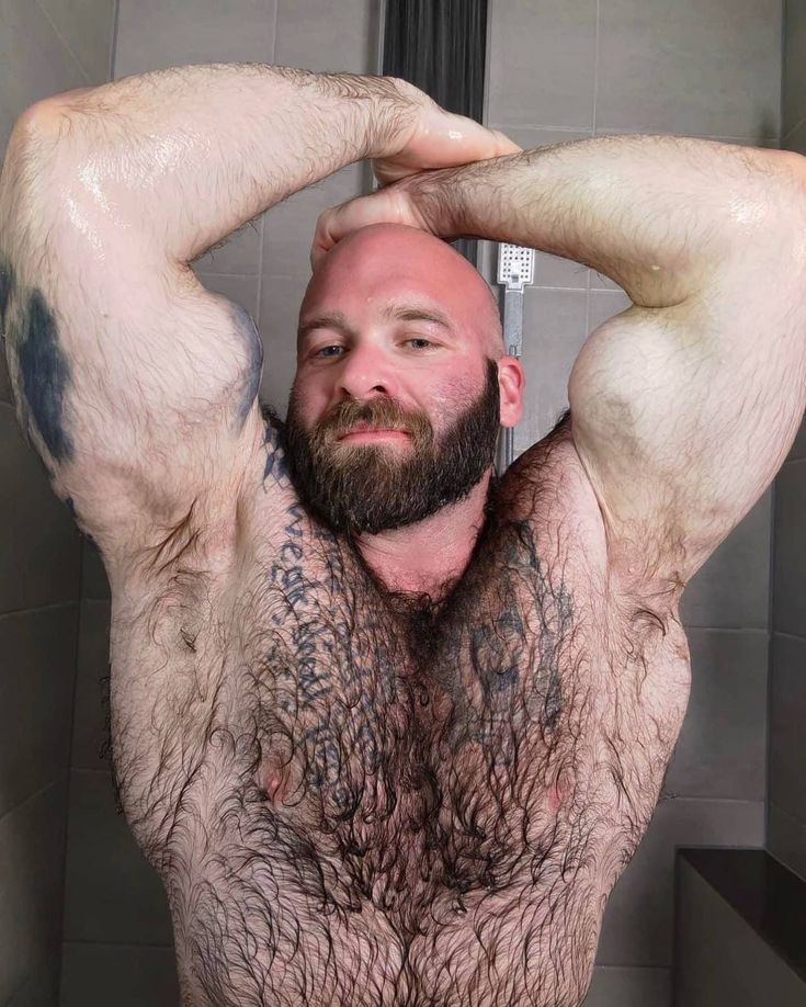 a man with tattoos on his chest standing in front of a shower