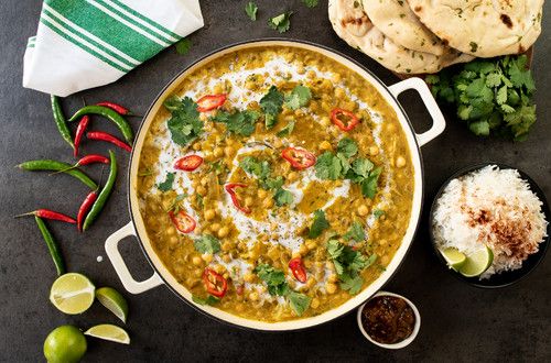 a pan filled with curry and rice next to some pita bread, cilantro